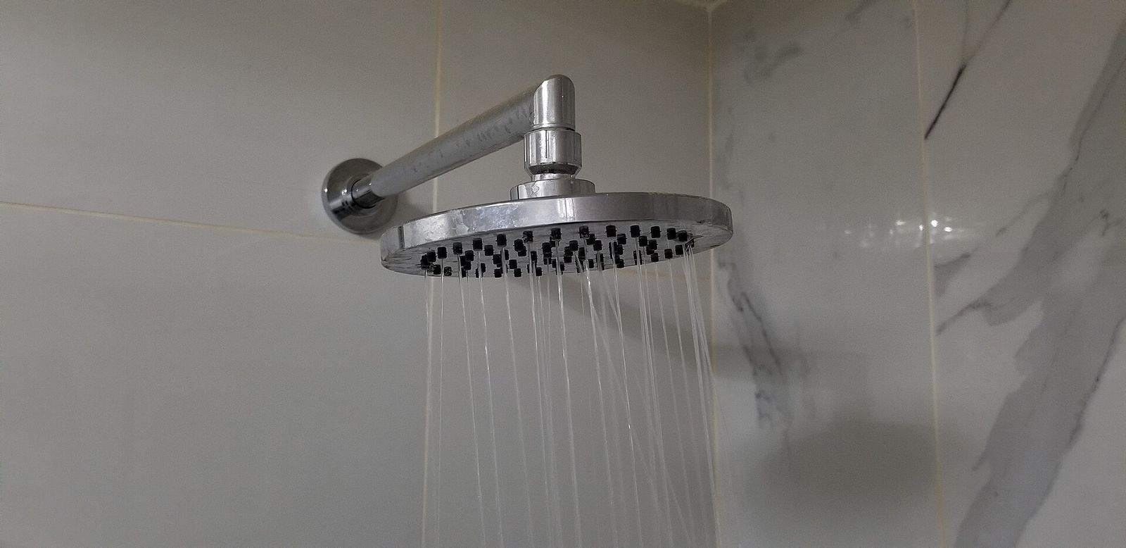 Soffione doccia a pioggia con acqua in funzione su parete rivestita in marmo