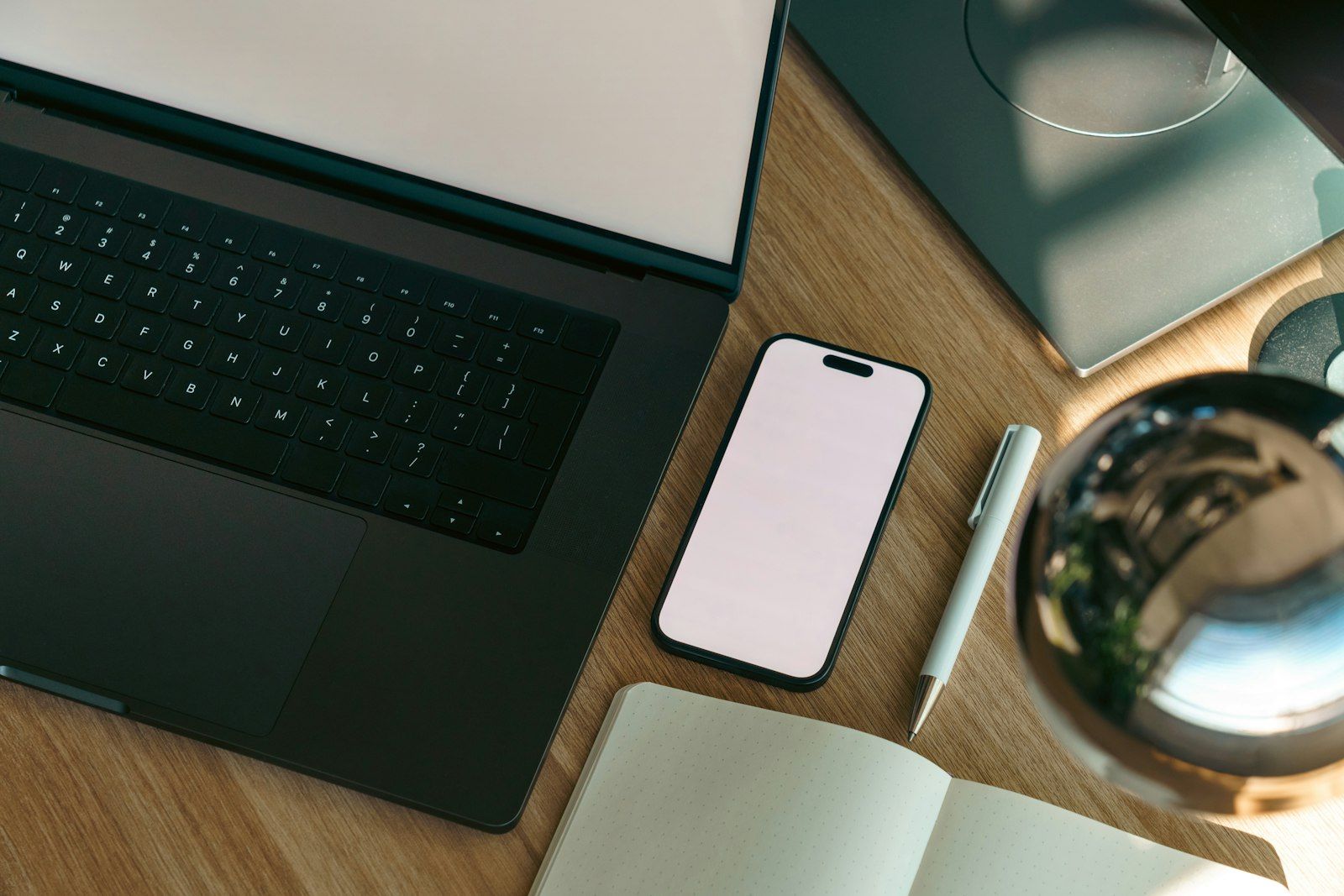 Computer portatile, telefono e taccuino su una scrivania in legno